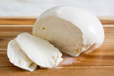 自制的新鲜马苏里拉奶酪球，切成半片，放在木砧板上。