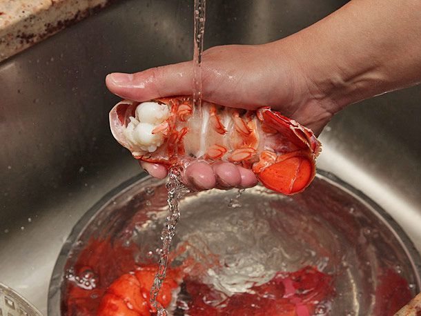 把煮熟的龙虾尾放在自来水下，下面放一碗水和龙虾的其他部位