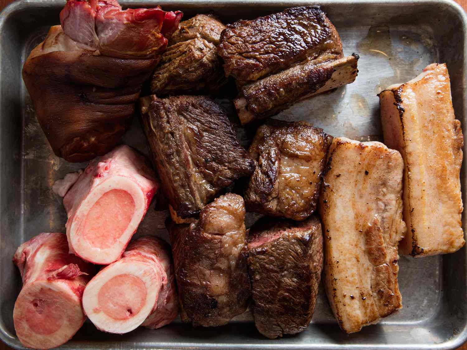 褐色的五花肉，牛短排骨，骨髓，烟熏的猪腿放在带边的烤盘上。gydF4y2Ba