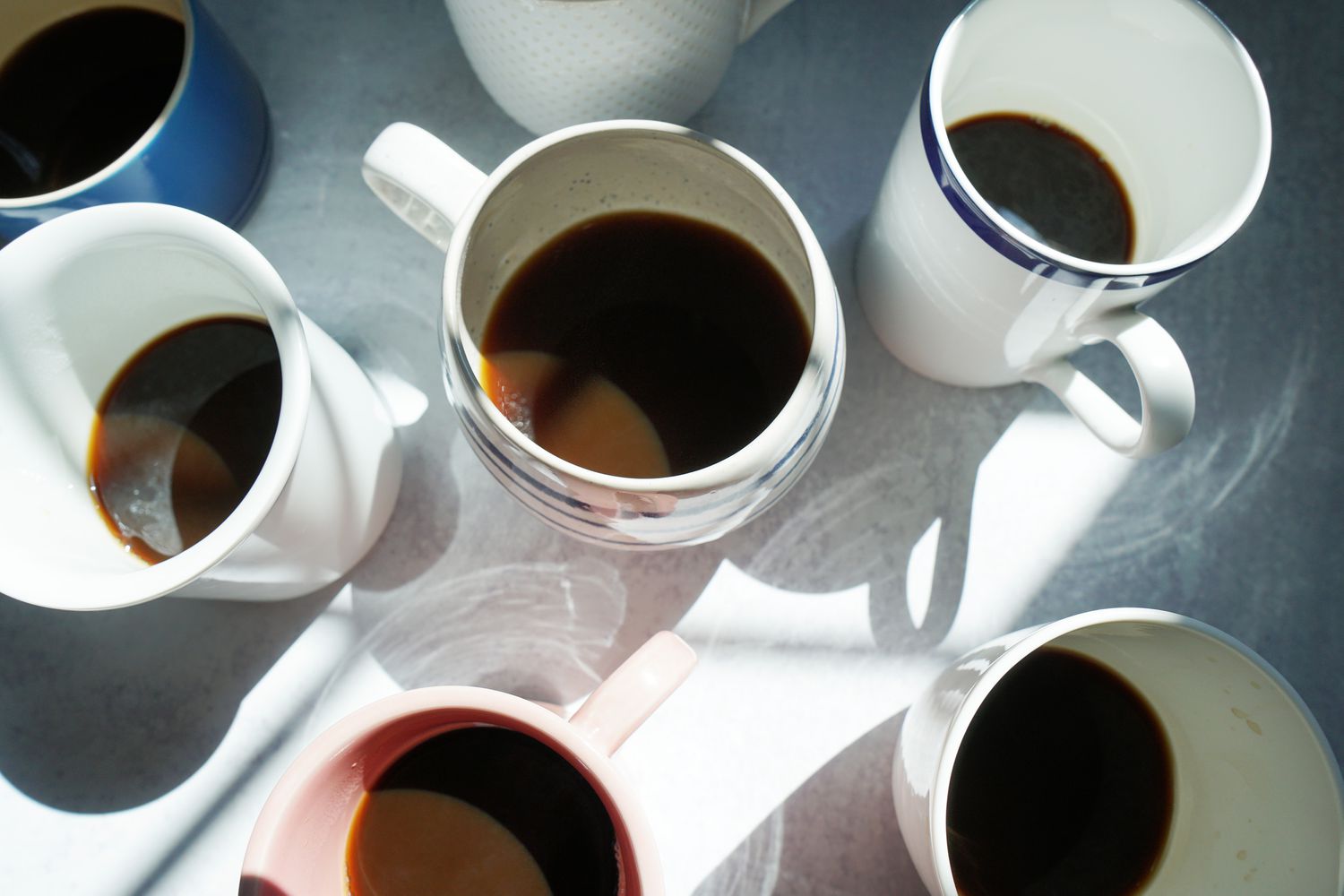 several mugs half full of coffee on a light grey surface