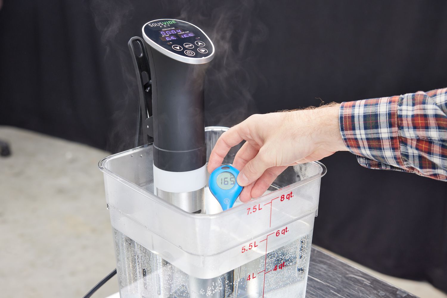 A sous vide machine heating up a cambro container filled with water and a hand with a thermometer taking the temperature of the water