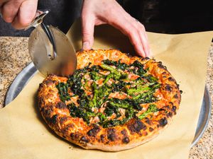 Slicing a pizza with charred broccoli rabe
