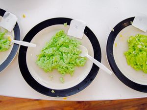 三个并排的盘子的炒鸡蛋和绿色食品色素染色。鸡蛋的味道和质量测试。