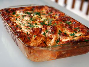 A rectangular glass baking pan of lasagna bolognese sprinkled with fresh chopped herbs.