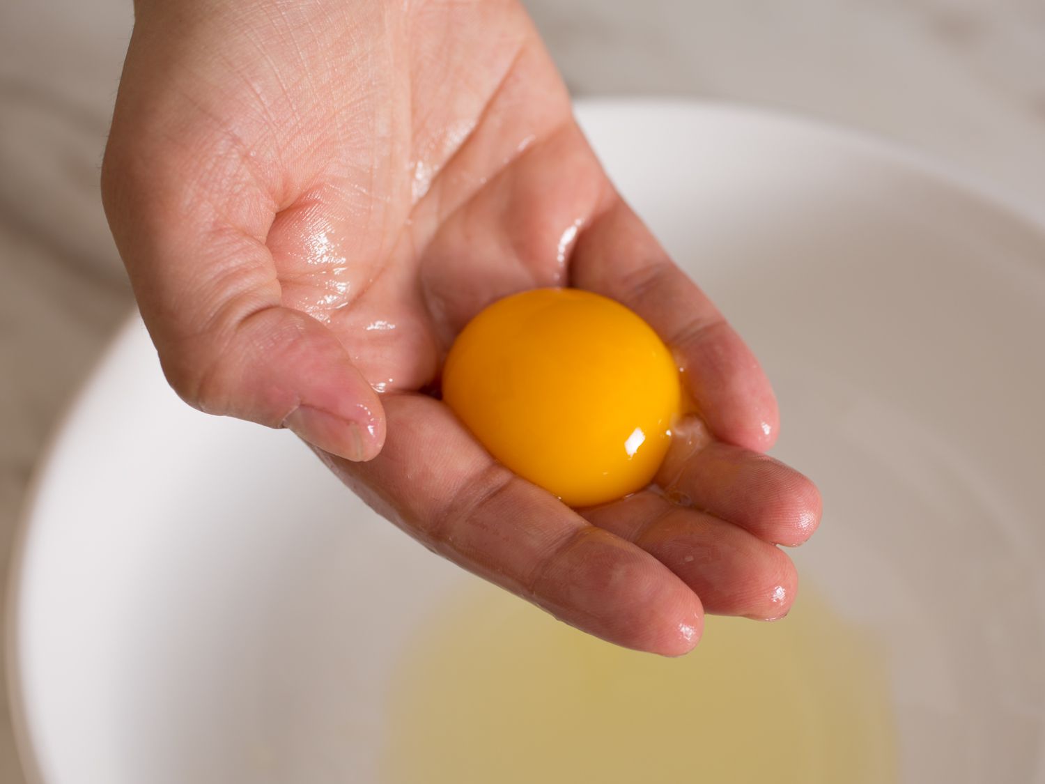 背景是一只手捧着白色碗里的蛋黄和蛋清。
