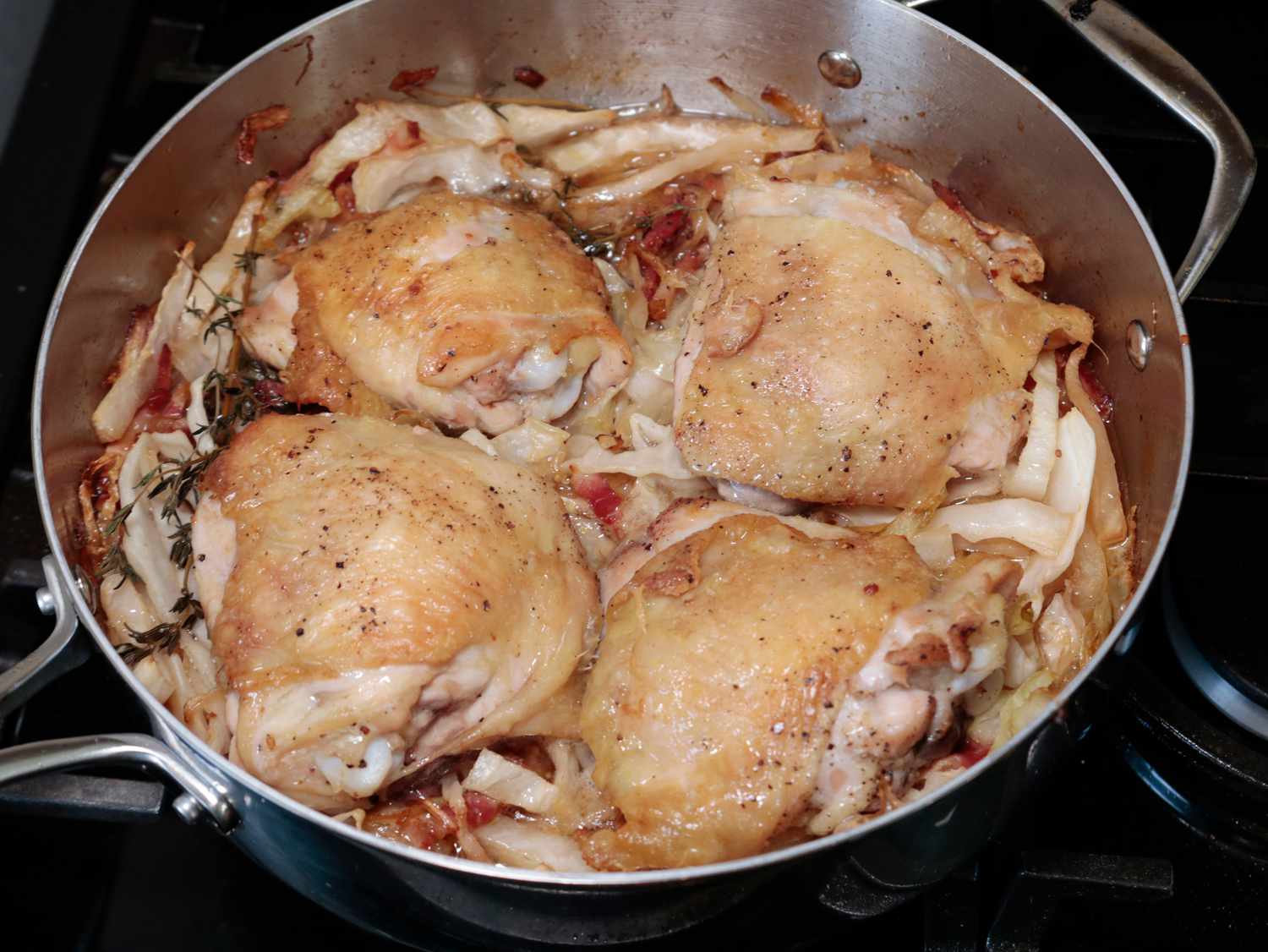 four chicken thighs braising on top of a bed of cabbage in a saute pan