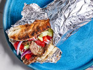 Greek-American Gryo wrapped in aluminum foil on a bright blue plate.