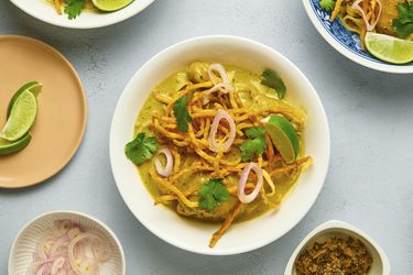 Khao soi gai in a white ceramic bowl, with additional small bowls containing condiments on the periphery.
