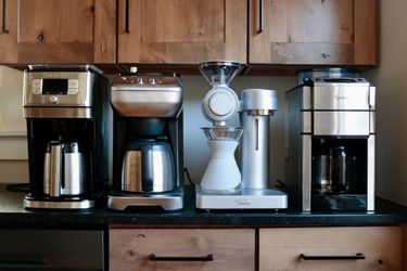 four coffee makers with built-in grinders lined up on a kitchen counter