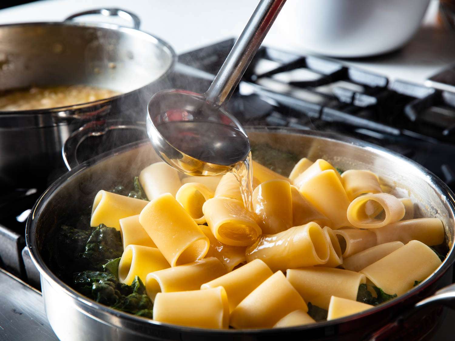 把水倒在平底锅里的意大利面和蔬菜上的长柄勺。