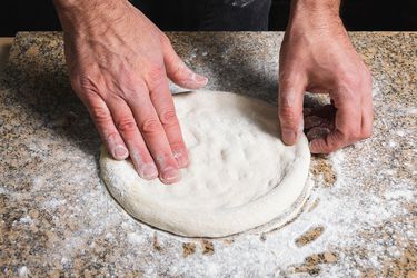 手在室外的披萨烤箱上捏着撒了面粉的披萨面团gydF4y2Ba
