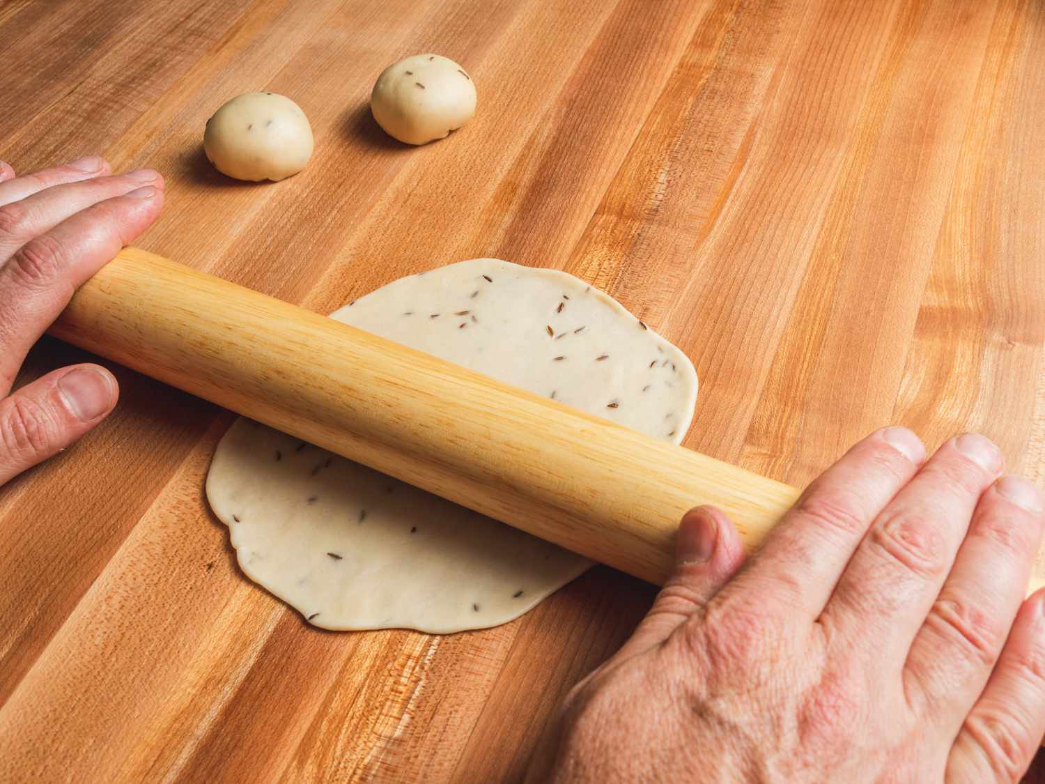Samosa dough ball being rolled out with a rolling pin into a circle