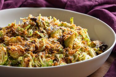 A bowl full of this salad, showing the varied textures of toasted breadcrumbs, thinly shaved raw Brussels sprouts, and crispy roasted ones, plus grated cheese, all lightly dressed in a creamy dressing.