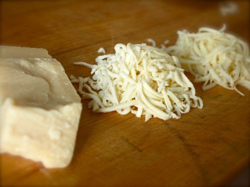 一堆切碎的切达奶酪和一块帕玛森奶酪放在木板上。gydF4y2Ba