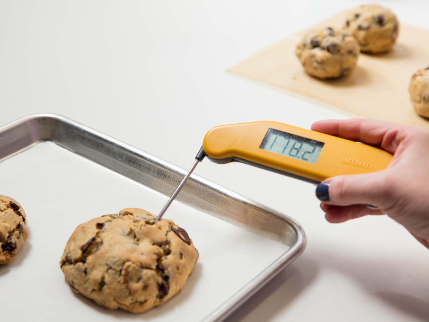 用探针温度计在羊皮纸衬里的烤盘上测量巧克力饼干的温度。gydF4y2Ba