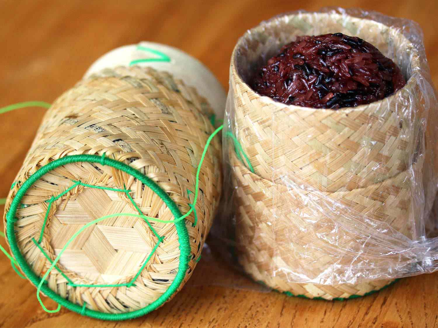 有盖的编织篮(thipkhao)，里面装着一堆深色的糯米粒(khao niew)。