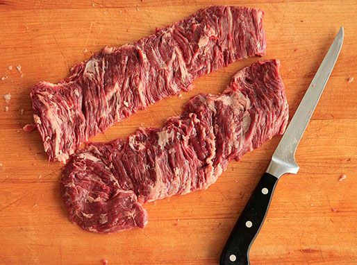 用切肉片的刀在木砧板上切生牛排。