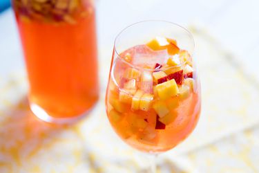 A glass of Sparkling Rosé Sangria With Aperol and Peaches, and a pitcher of the cocktail in the background.