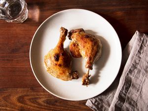 两只油封鸭腿，真空烹饪，然后烤，放在一个白色的盘子上，旁边放着一张灰色的餐巾和一杯水。