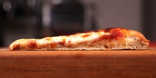 纽约风格的披萨切片的横截面，面团不发达，显示出扁平的纹理和隆起。gydF4y2Ba