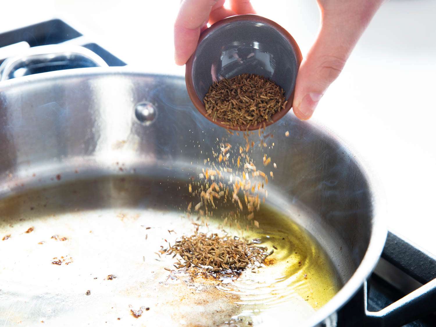 一只手从一个小碗里往sauté平底锅里加入孜然籽