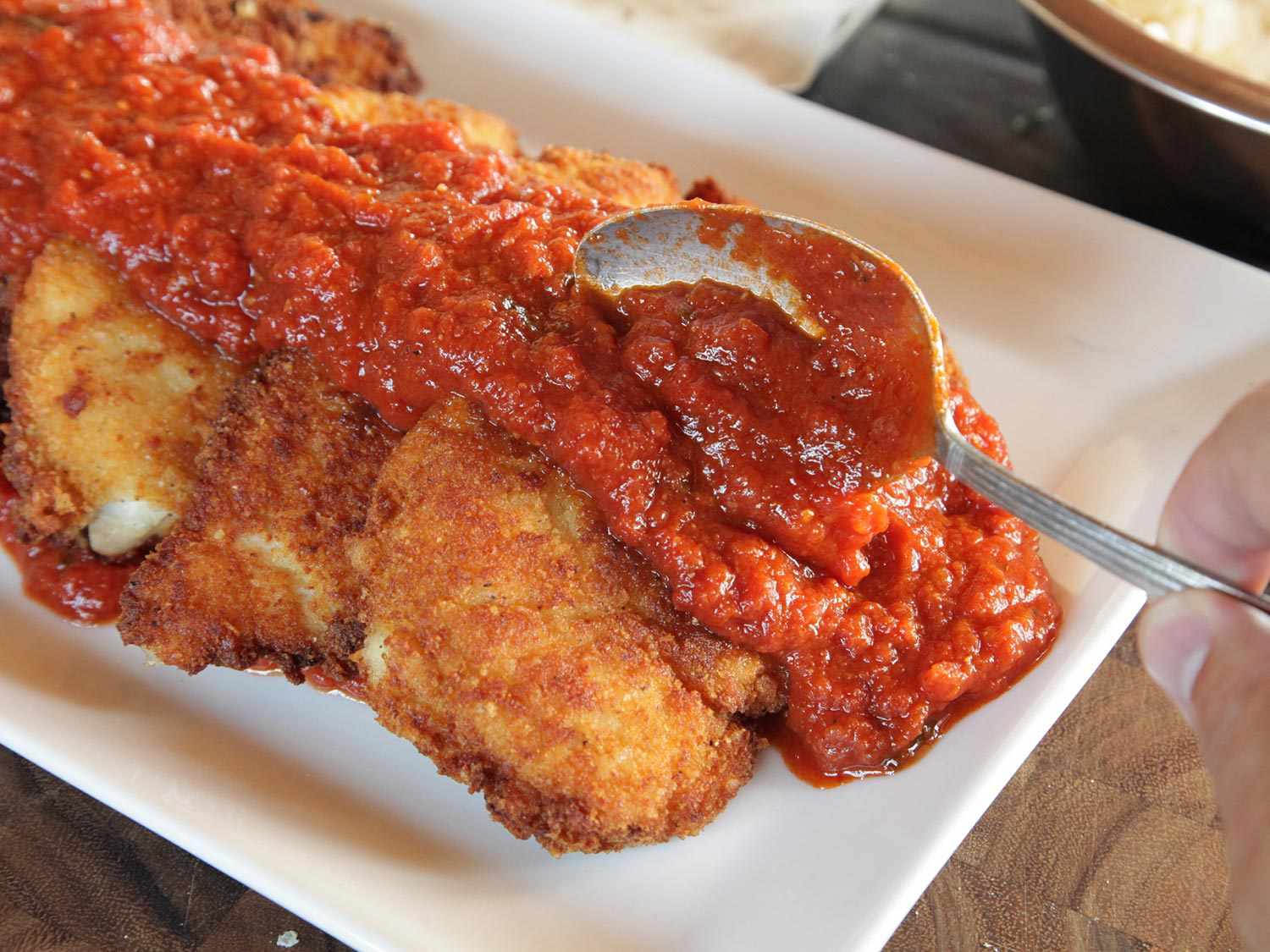 Spooning red sauce over fried chicken breasts