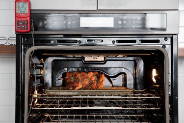 A chicken roasting inside an oven with a probe thermometer panel on the outside of the oven