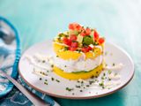 Layered dish of yellow mashed potatoes and tuna salad topped with diced tomatoes and avocados