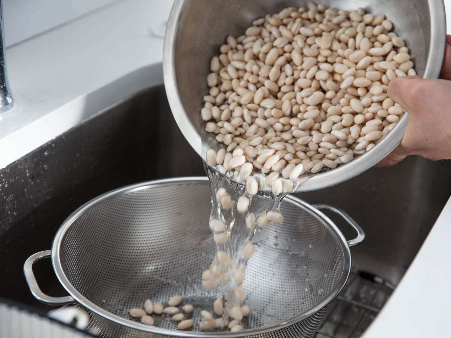 将一大碗浸泡过的白豆倒入水槽的滤锅中