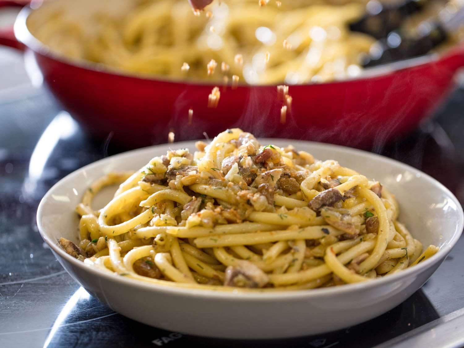 Sprinkling additional breadcrumbs over a finished dish of Sicilian pasta with sardines.