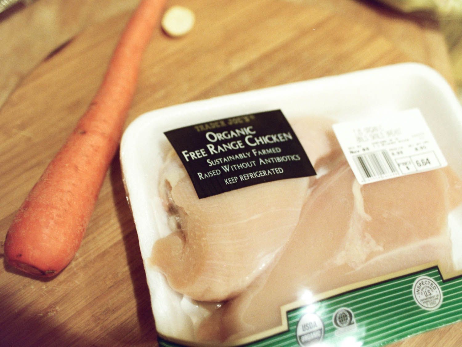 有机去皮的鸡胸肉包在一个木砧板一个胡萝卜。
