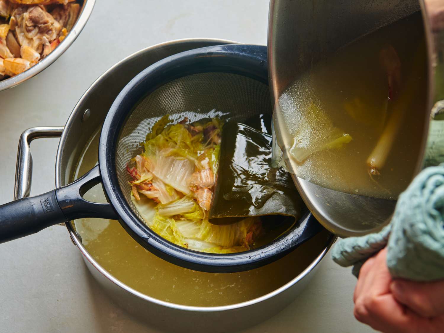 汤汁从汤锅中通过细网过滤器过滤到另一个小锅中。