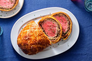 Beef Wellington on an oval white ceramic plate, with two slices of Wellington on the right hand side of the plate.