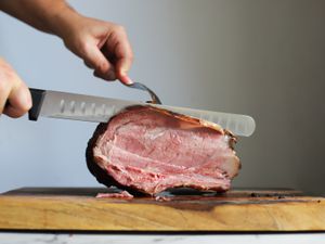 一只手用切片刀切下一块最好的肋骨烤坐落在一个木制的砧板