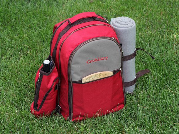 一个红色的背包野餐篮,酒瓶,一条毯子,和一个小砧板。