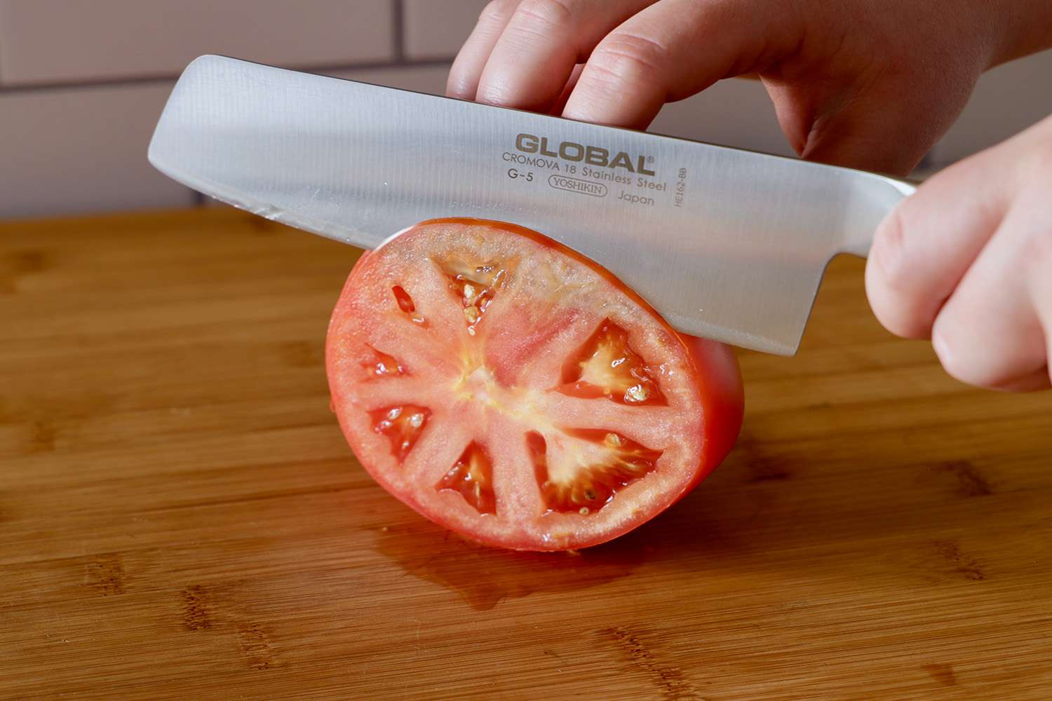 两只手用刀把番茄切成薄片放在砧板上