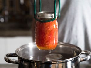 用钳子从水浴中取出一罐加工过的西红柿。