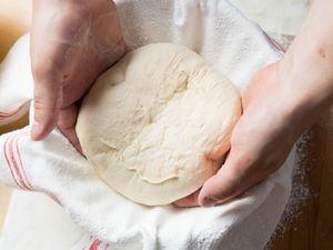 两只手将球的面包面团成一碗用磨碎的厨房毛巾。
