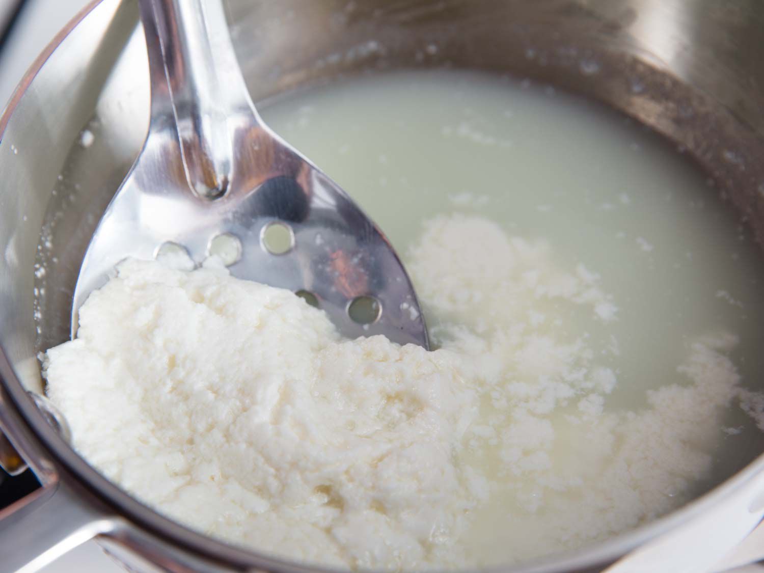 用勺子舀起要过滤的牛奶凝乳来做乳清干酪。