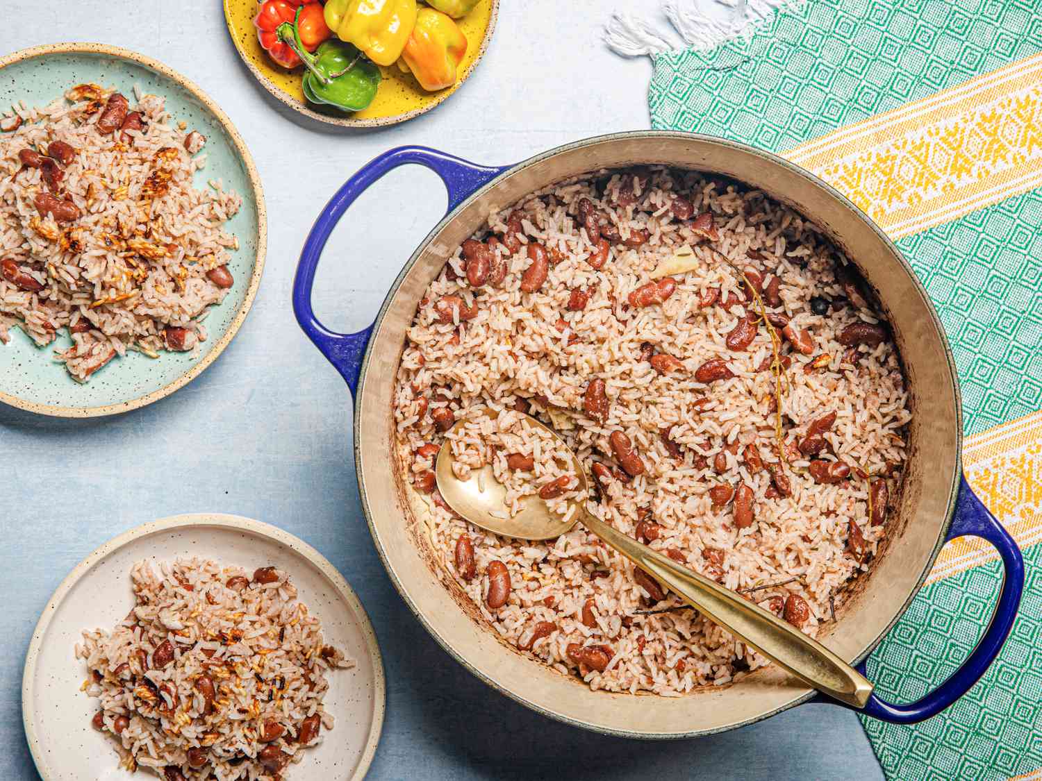 一锅牙买加米饭和豌豆的俯视图，有一个勺子，两个盘子和一个绿色和黄色的织物