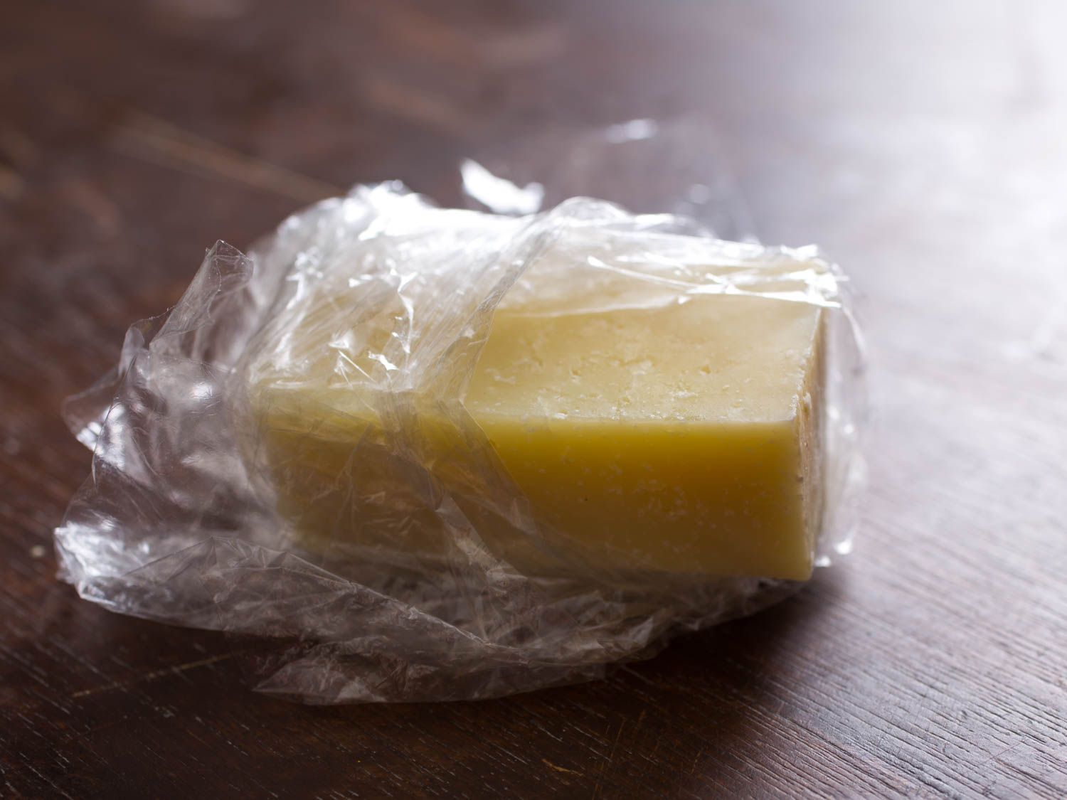 一块被保鲜膜包裹得很糟糕的奶酪，有些奶酪暴露在外。