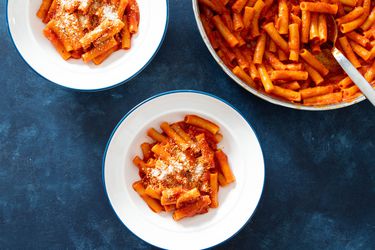 Overhead shot of two white bowls filled with pasta with tomato sauce next to pot of pasta