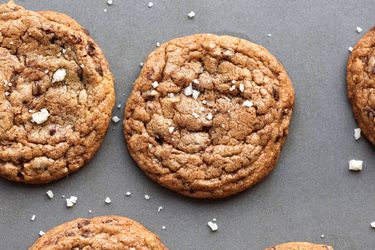 An array of chocolate chip cookies on a grey background sprinkled with flaky salt.