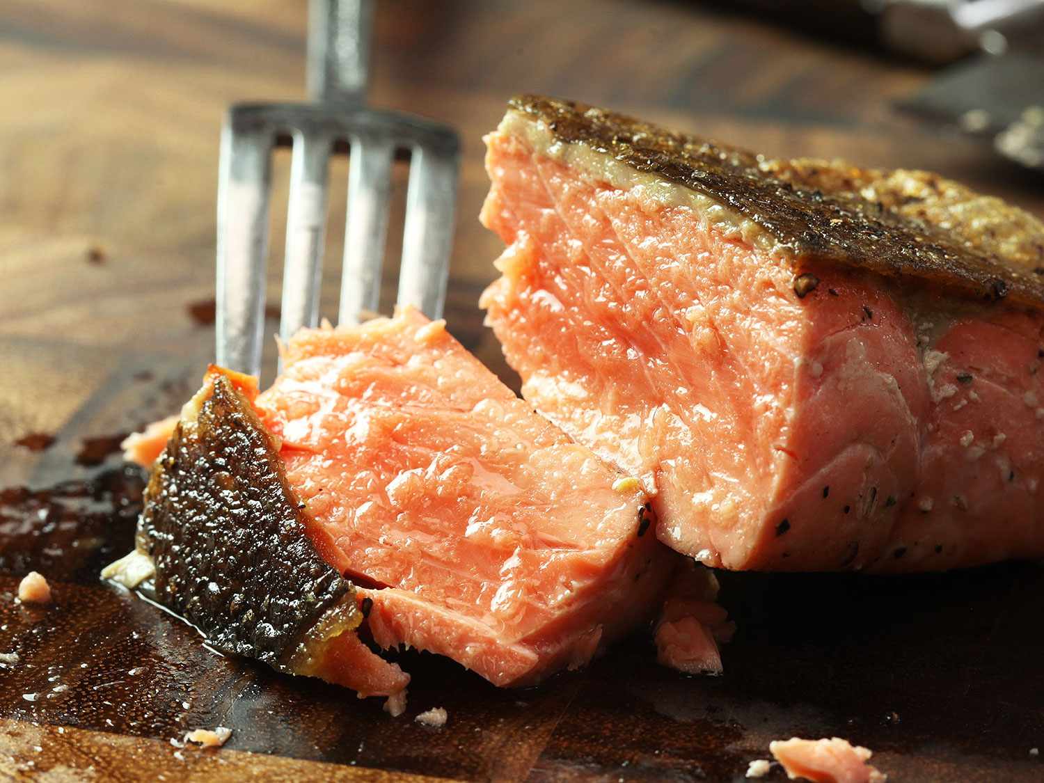 用叉子咬一口放在木砧板上的脆皮烤鲑鱼片。