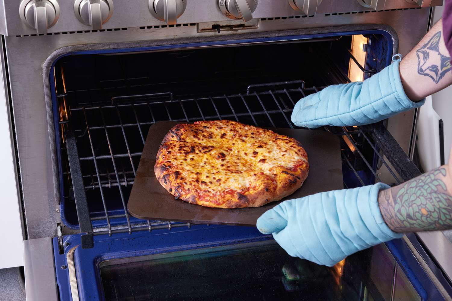 最初的烤箱烘烤钢也被拉去和一个煮熟的披萨的人穿着烤箱手套