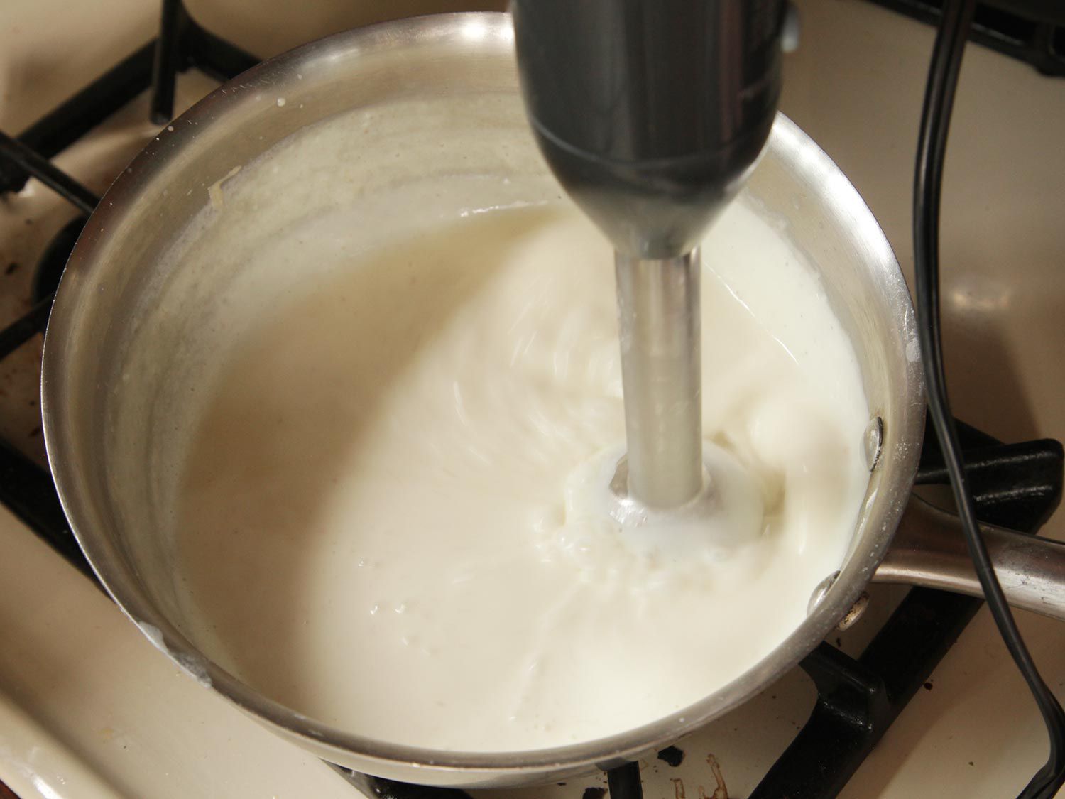用浸入式搅拌器把白酱汁里的块状搅匀。