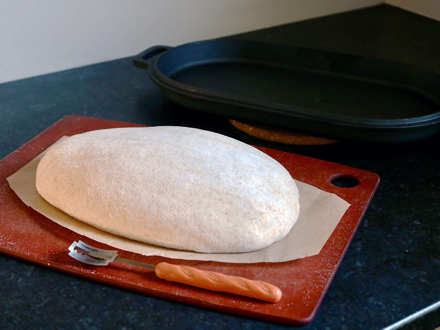 一块生面团放在砧板上，旁边是一个面包板和一个铸铁平底锅的底部。