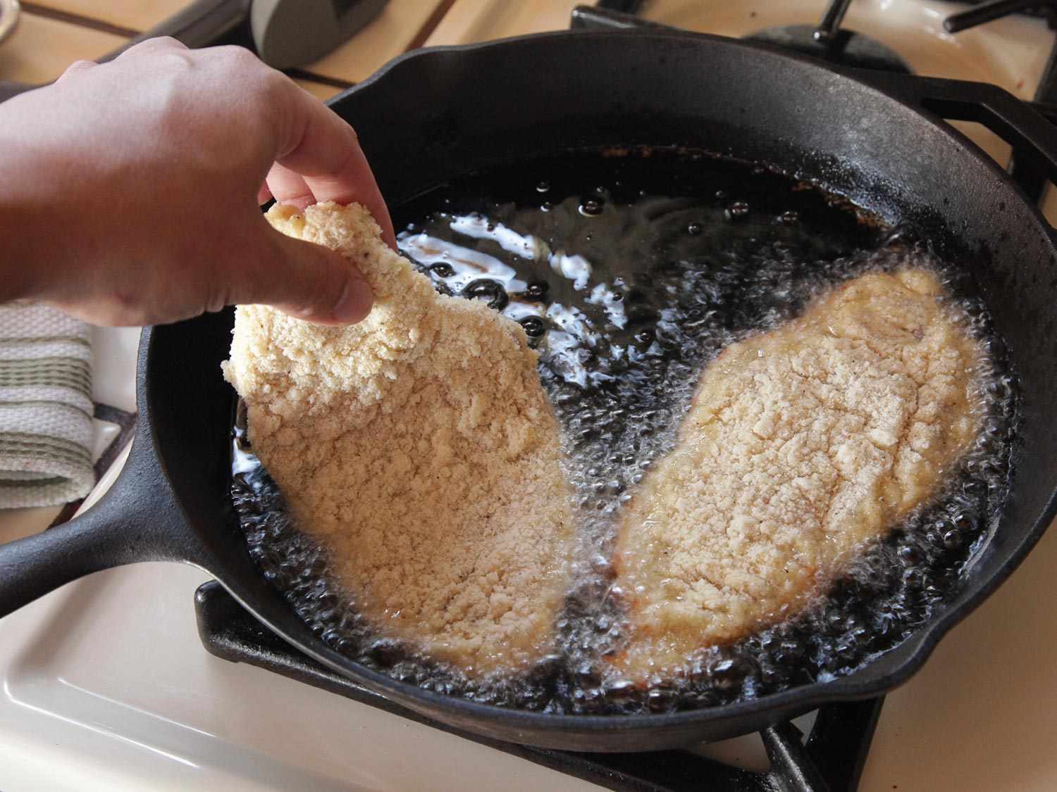 Lowering breaded chicken breast into cast iron skillet of hot oil