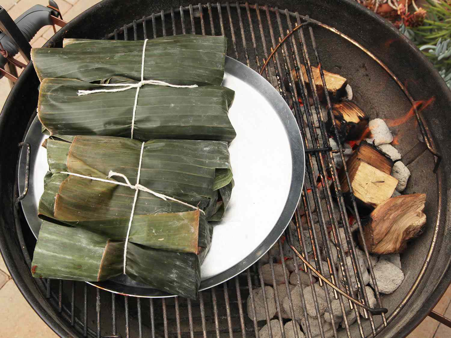 Roasting banana leaf-wrapped pork on a grill over indirect heat.