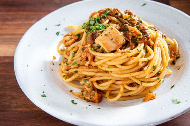 Roman-style spaghetti alla carrettiera, with tomatoes, tuna, porcini mushrooms, and more, piled on a plate and sprinkled with fresh parsley